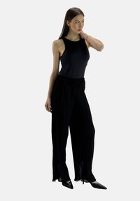 Zwarte mouwloze top gecombineerd met brede zwarte plissébroek met een taillekoord. Model draagt puntige zwarte schoenen. Eenvoudig, elegant ontwerp.