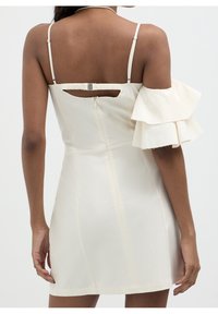 Bílé šaty s přiléhavým střihem, volnými rukávy s volány, výstřihem na zádech a zapínáním na zip na zadní straně.