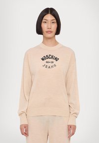 Sweater bege com decote redondo canelado e mangas compridas. Apresenta o logótipo preto "MOSCHINO JEANS 86-23" na frente. Textura suave.