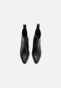 Paire de bottines en cuir noir à bouts pointus et languettes d'extraction, vues de dessus sur un fond clair.