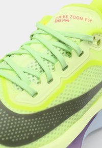 Nike Zoom Fly sneakers feature a bright neon yellow upper with mesh panels, grey accents, and flat laces. Lightweight design with a curved sole.