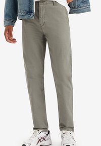 Pantalones gris claro en una mezcla de algodón con un diseño de pierna recta. Presentan bolsillos delanteros y un cierre de cremallera. Combinados con zapatillas blancas.