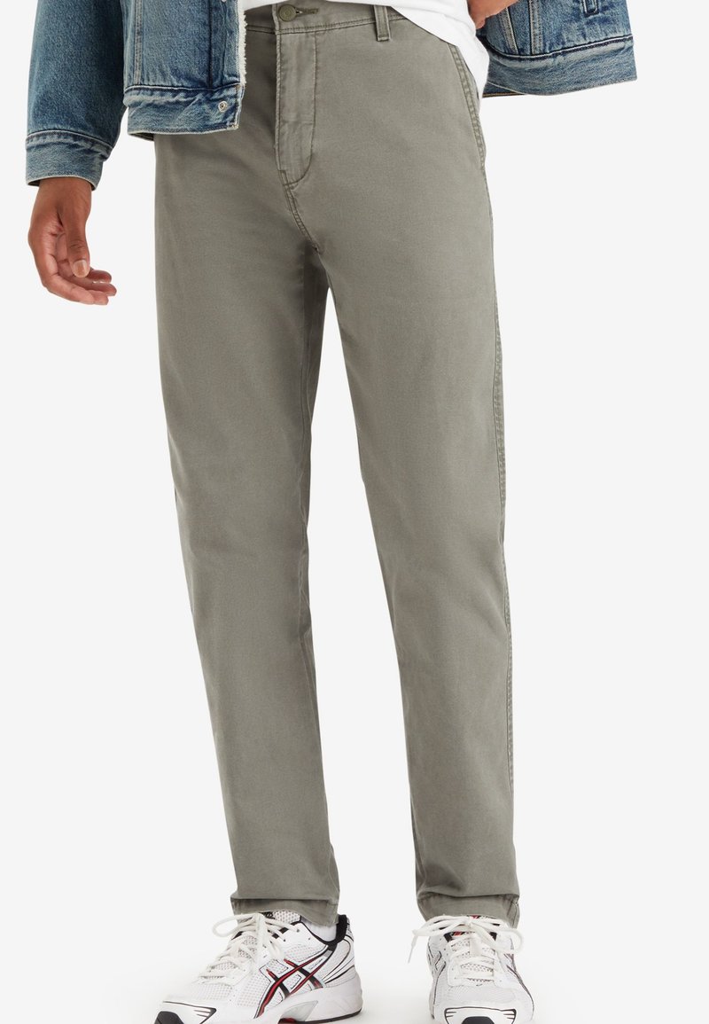 Pantalons gris clair en mélange de coton avec une coupe droite. Dotés de poches avant et d'une fermeture éclair. Assortis à des baskets blanches.