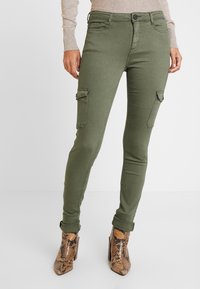 Pantalons cargo vert olive avec une coupe ajustée, dotés de poches latérales et d'une texture lisse, associés à des bottes à chevilles marron à motifs.