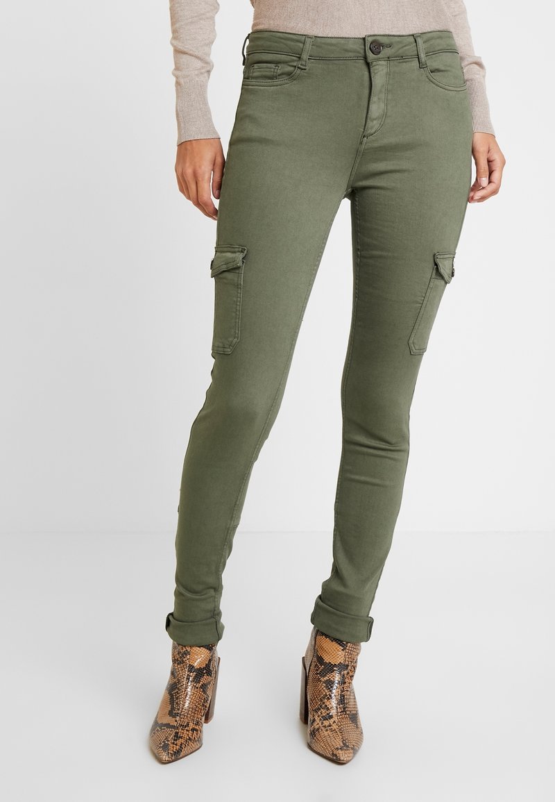 Pantalons cargo vert olive avec une coupe ajustée, dotés de poches latérales et d'une texture lisse, associés à des bottes à chevilles marron à motifs.