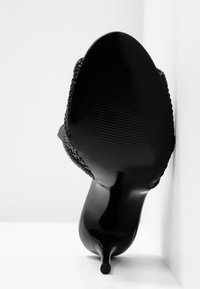 Semelle de chaussure en cuir noir à talon kitten avec partie supérieure tressée, vue de dessous sur fond blanc.