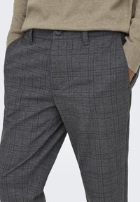 Graue Karohosen aus strukturiertem Stoff, mit Knopfverschluss und Seitentaschen, in taillierter Passform für eine gestraffte Silhouette.