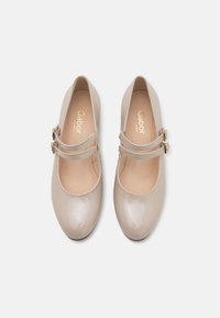 Chaussures Mary Jane en cuir verni beige avec bouts arrondis, doubles brides et boucles dorées, vues de dessus sur fond blanc.