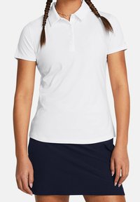 Biała koszulka polo z kołnierzykiem i krótkimi rękawami, wykonana z gładkiego materiału. Zestawiona z granatową spódnicą w fasonie kopertowym.