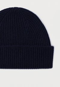 Laivastonsininen neulottu villapipo, jossa on ribbineuloskuvio ja käännetty reuna, asetettuna tasaisena valkoista taustaa vasten.