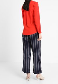 Blouse rouge à manches longues associée à un pantalon large bleu marine à rayures. Le pantalon présente des rayures verticales rose et blanc. Finition du tissu lisse.