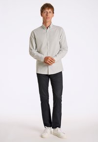 Camisa de botones a rayas en verde claro y blanco, combinada con pantalones oscuros y zapatillas blancas. Tela suave con un diseño ajustado.