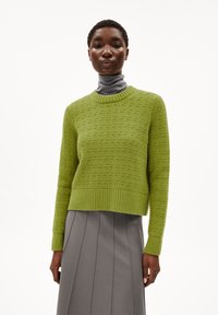 Groene gebreide trui met een textuurpatroon, ronde hals en geribbelde zoom. G gedragen over een grijze coltrui en gecombineerd met een geplooide grijze rok.
