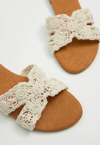 Sandalias de ante marrón claro con correas decorativas de macramé de color crema. Las correas presentan patrones en espiral y tienen un diseño plano y abierto en la parte delantera.