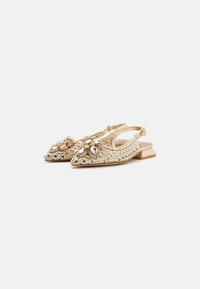 Zapatos slingback dorados con tacón cuadrado, que presentan adornos florales decorativos y rhinestones de diferentes tamaños en la zona de los dedos.