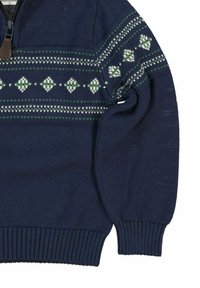 Neulepaita tummansinisenä, jossa on korkea kaulus ja vetoketju. Rinnassa ja hihoissa on vaaleanvihreä ja valkoinen geometrinen kuvio.