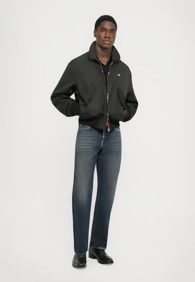 Black bomber jacket with a high collar, two front pockets, and a zip closure; paired with dark blue straight-leg jeans and black shoes.