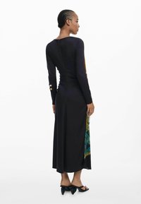 Robe noire à manches longues avec un design ajusté, présentant un panneau latéral coloré, une fermeture éclair discrète au dos et des talons glissés minimalistes et élégants.