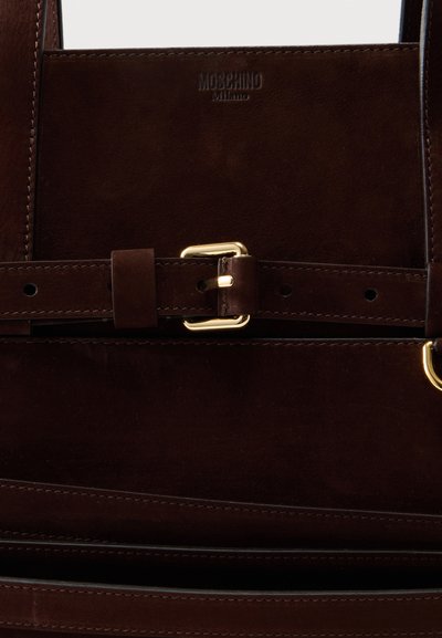Εσωτερικό τσάντας Moschino Milano από σκούρο καφέ δέρμα με ραμμένο λουράκι και λεπτομέρειες με αγκράφα σε χρυσό τόνο.