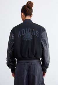 Zwarte bomberjack met gestructureerde stof, leren mouwen en geborduurd "ADIDAS" en rozenontwerp op de achterkant. Ribgebreide manchetten en zoom.