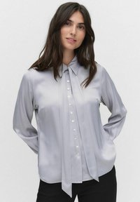 Hellgraue Bluse mit Kragen, langen Ärmeln und Knöpfen vorne. Verfügt über eine gefältelte Detail und eine glatte Satinoberfläche.