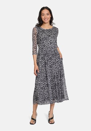 Maxikleid mit schwarzem Leopardenmuster auf transparenter Stoff, dreiviertellange Ärmel, A-Linien-Silhouette und Seitentaschen. Tragen von schwarzen Sandalen.
