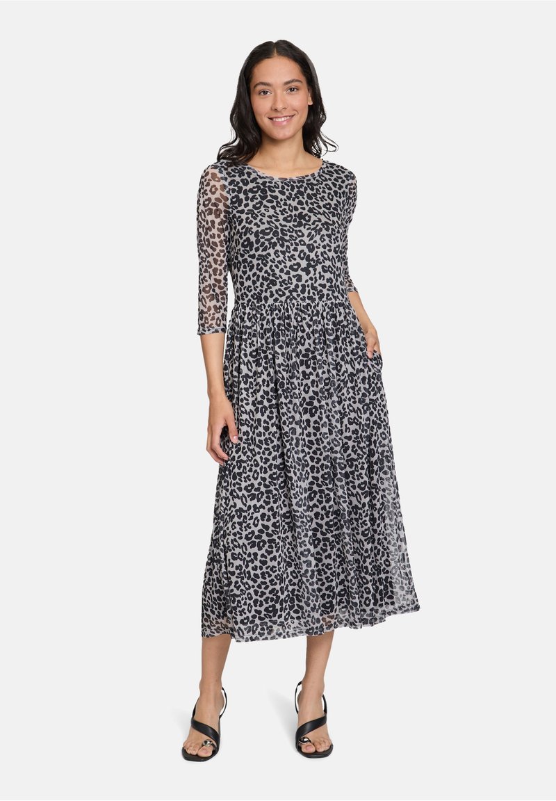 Maxikleid mit schwarzem Leopardenmuster auf transparenter Stoff, dreiviertellange Ärmel, A-Linien-Silhouette und Seitentaschen. Tragen von schwarzen Sandalen.