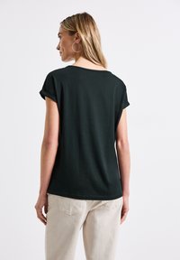 Mörkgrön t-shirt med kort ärm, avslappnad passform, uppvikta ärmar och rundad nederkant, tillverkad av mjuk och andningsbar tyg.
