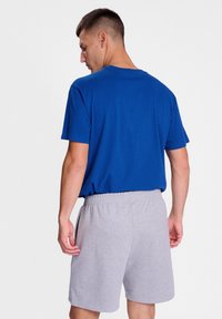 Blå bomullströja med korta ärmar i kombination med ljusgrå shorts med elastisk midja. Klädseln verkar avslappnad och bekväm.