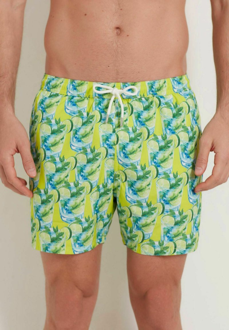 Vihreät ja keltaiset uimapuvut, joissa on toistuva kuvio trooppisista juomista, limeviipaleista ja mintunlehdistä. Nyörivyöt mukana.