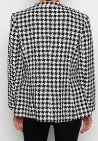 Blazer med svart och vitt hundtandsmönster, med skräddarsydd passform, texturerad tyg, notchad krage och långa ärmar.