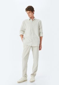 Camisa de botones a rayas en beige claro con mangas enrolladas, combinada con pantalones beige claro y zapatillas crema. Tejido suave y texturado.