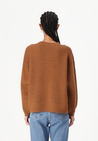 Brown ribbed knit sweater with a relaxed fit, rounded neckline, and dropped shoulders. Paired with light-wash denim jeans.