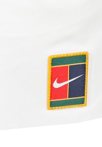 Parche del logo de Nike sobre un fondo de tela blanca, que presenta un diseño rectangular con secciones en rojo, verde y azul marino, bordado en hilo dorado.