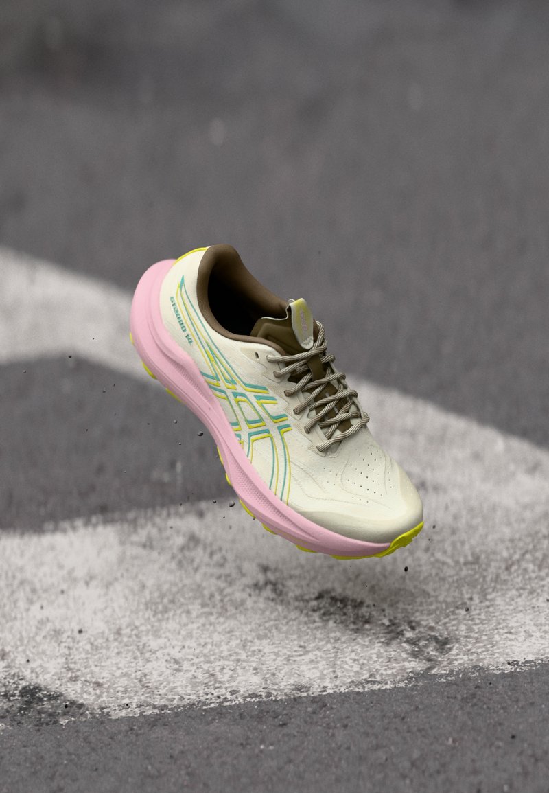 Ανοιχτό μπεζ αθλητικό παπούτσι για τρέξιμο με ροζ σόλα και κίτρινες λεπτομέρειες. Διαθέτει διαπερατό επάνω μέρος, κλείσιμο με κορδόνια και πολύχρωμες πλευρικές ρίγες.