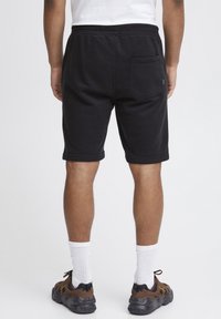 Pantalones cortos de algodón negros con cintura elástica, bolsillo lateral y dobladillos enrollados, combinados con zapatos marrones y calcetines blancos de caña corta.