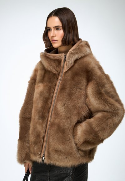 Brown faux fur jacket featuring a hood, zip closure, and wide sleeves. Soft texture with contrasting brown accents. Styled with a black skirt.