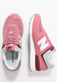 Tenisky New Balance v růžové semišové a síťované úpravě, s šedými akcenty a bílým logem, s texturovanou gumovou podrážkou a polstrovaným límcem.