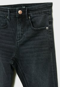 Jeans de mezclilla negra ajustados, con un botón de cobre, cinco bolsillos y detalles de costura en gris a lo largo de las costuras. Talla 34.