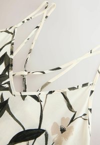 Blommönstrad topp i lätt material med spaghetti band. Bakgrunden har krämfärgade och svarta botaniska motiv med beige blommor.
