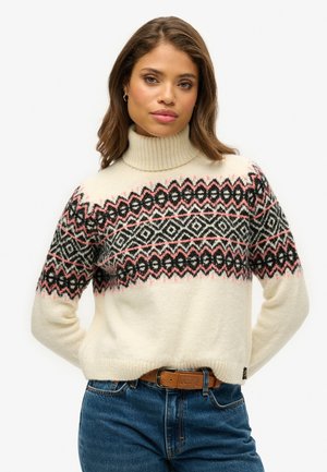 Crème col roulé trui van zacht materiaal, met een geometrisch zwart, wit en roze patroon op de borst, en geribbelde manchetten en onderrand.