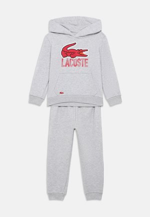 Conjunto de hoodie e calças para crianças em cinza claro, com o logótipo do crocodilo da Lacoste em vermelho e texto no peito, punhos canelados e bolso frontal tipo canguru.