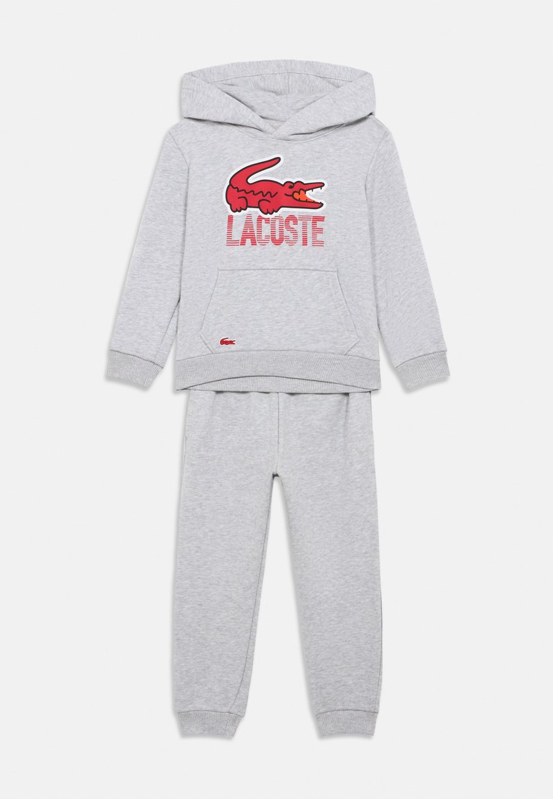 Conjunto de hoodie e calças para crianças em cinza claro, com o logótipo do crocodilo da Lacoste em vermelho e texto no peito, punhos canelados e bolso frontal tipo canguru.