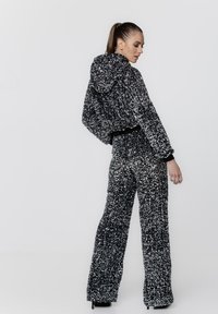 Czarny i srebrny dres z cekinami, z krótką bluzą z kapturem i szerokimi spodniami. Teksturowana powierzchnia; dopasowany w talii z elastycznym pasem.