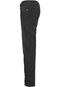 Jean noir slim fit montré de profil avec poches avant et arrière visibles, passants de ceinture et légers détails de texture sur le tissu.