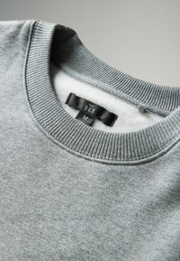 Szara bluza z prążkowanym dekoltem i dolnym obszyciem, wykonana z miękkiego materiału. Wewnątrz metka z nazwą marki "THE SET" oraz rozmiarem "M".