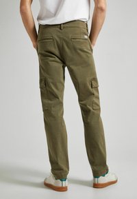 Olivgröna cargo-byxor med rak bendesign, som har bakfickor och sidofickor för cargo. Bärs med vita sneakers.