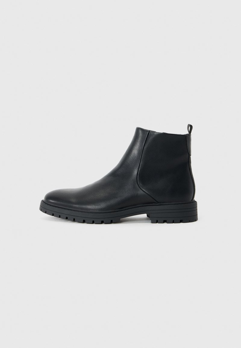 Botas de tobillo de cuero negro con un acabado suave, punta redondeada, tacón cuadrado y suela texturizada para agarre. Presentan una cinta en la parte posterior.