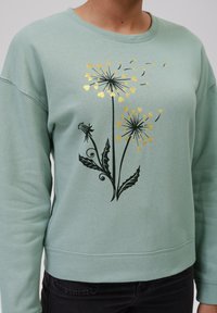 Mentolová mikina s černým květinovým vzorem a zlatými akcenty. Má kulatý výstřih a žebrované manžety, vyrobena z měkké látky.