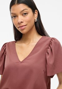Blusa rosa polverosa con maniche a sbuffo corte e scollatura a V. Realizzata in un tessuto leggero con una consistenza morbida e liscia.
